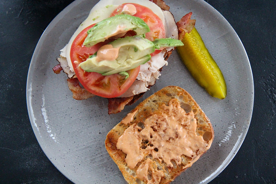 turkey and cheese sandwich with bacon and a pickle on a gray plate 