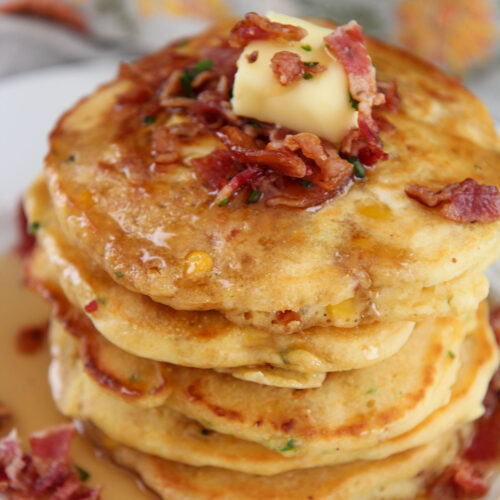 a short stack of bacon and corn pancakes on a white plate with syrup on top.