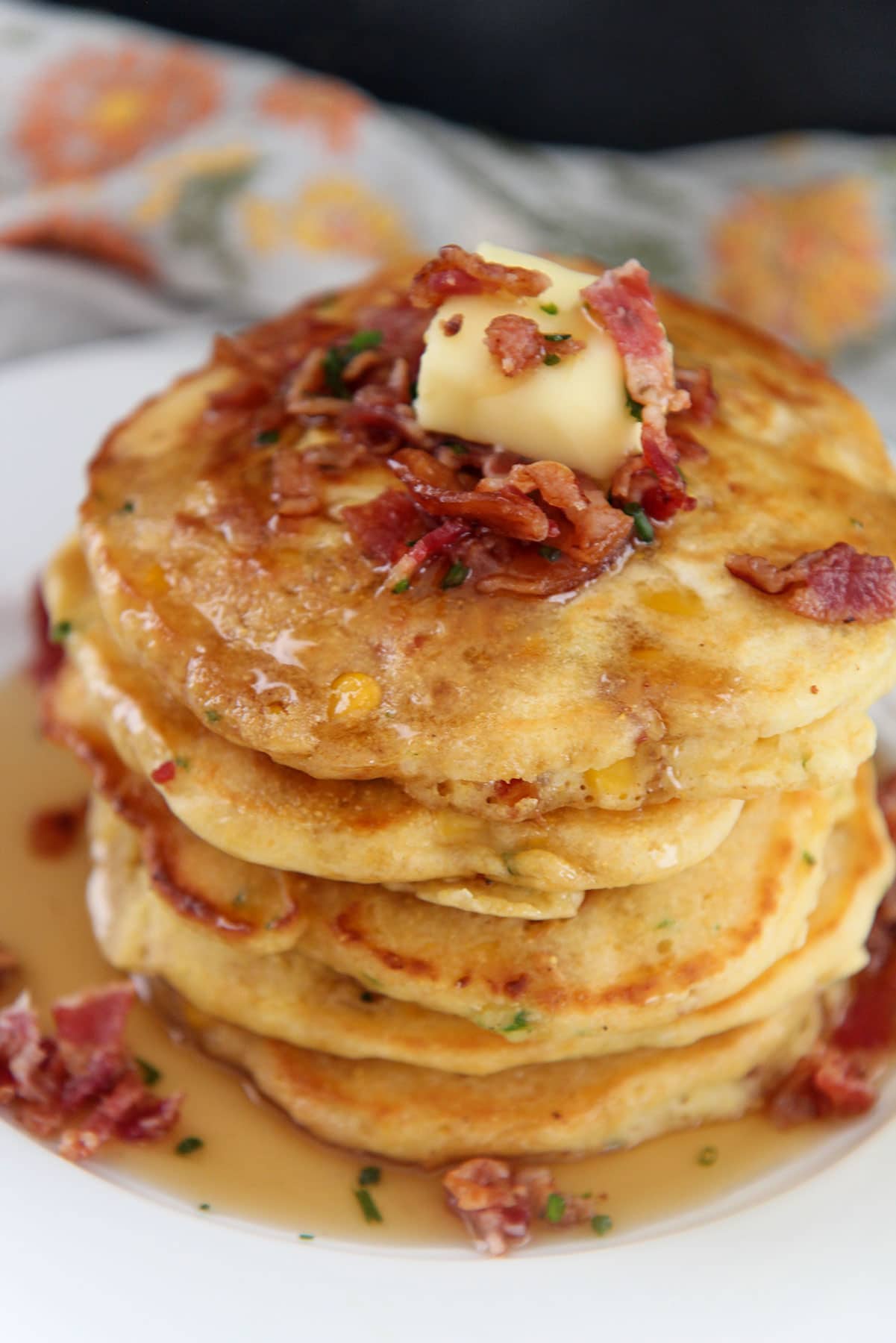 a short stack of bacon and corn pancakes on a white plate with syrup on top.