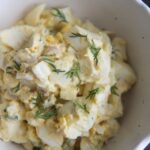 classic egg salad in a white bowl with fresh dill on top