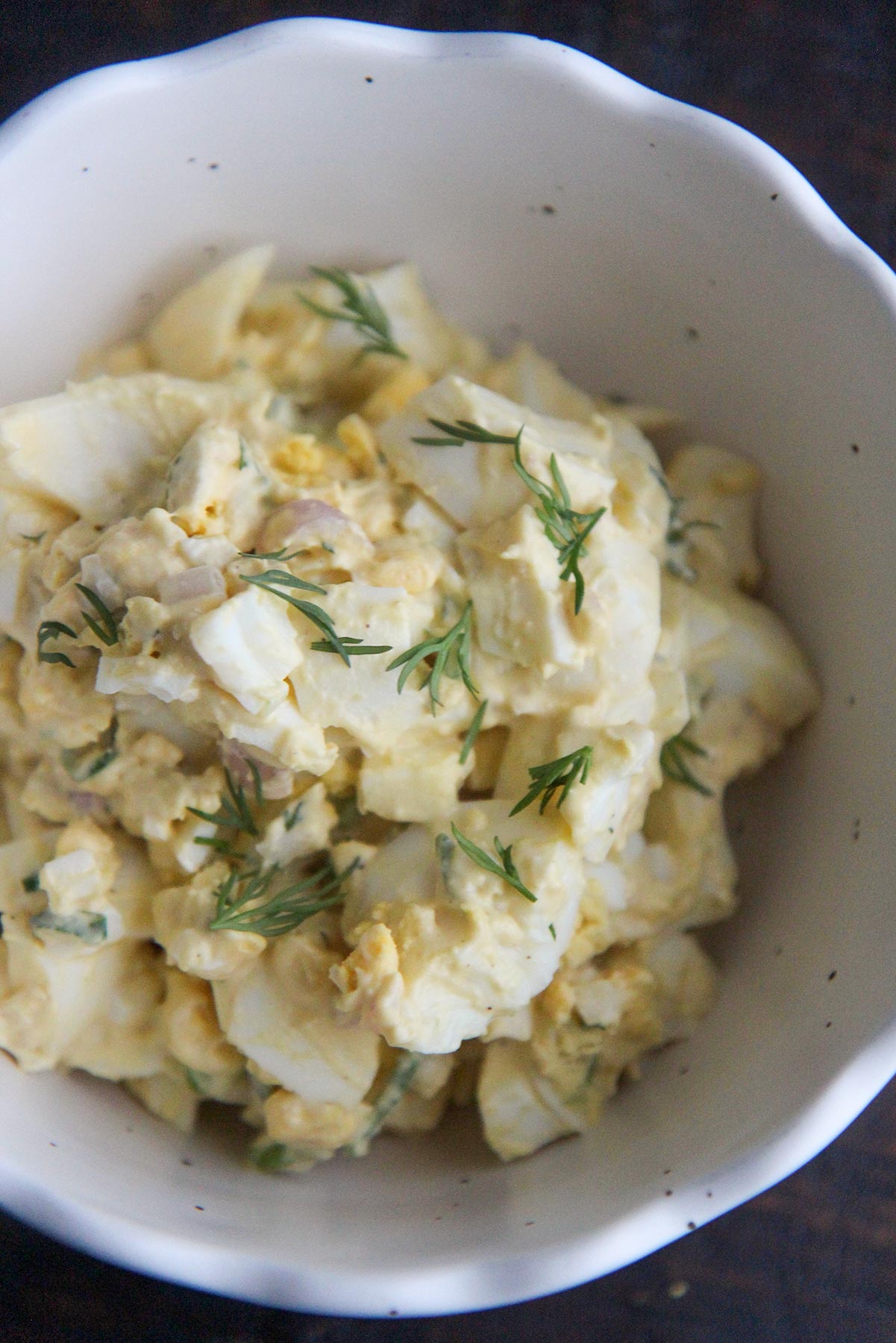 classic egg salad in a white bowl with fresh dill on top 