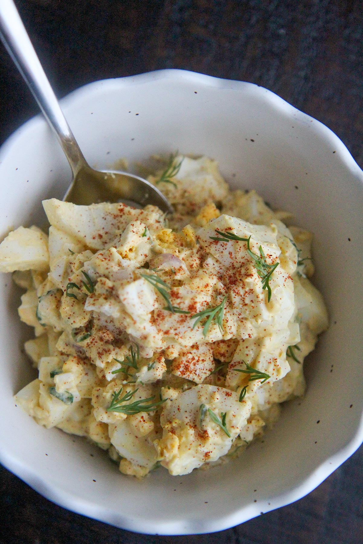 egg salad in a bowl with a spoon and paprika on top 