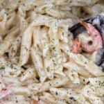 Shrimp and pasta covered in sauce with parsley and a wooden spoon up close.