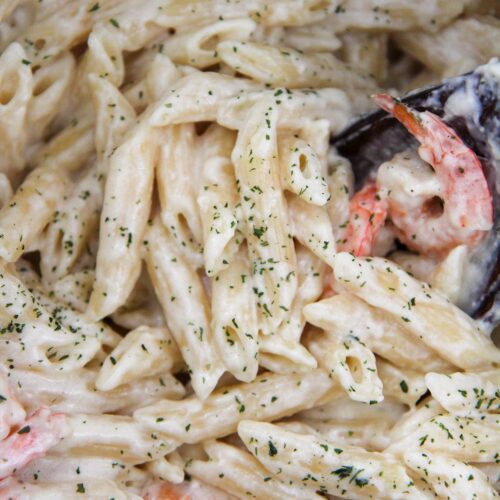 Shrimp and pasta covered in sauce with parsley and a wooden spoon up close.