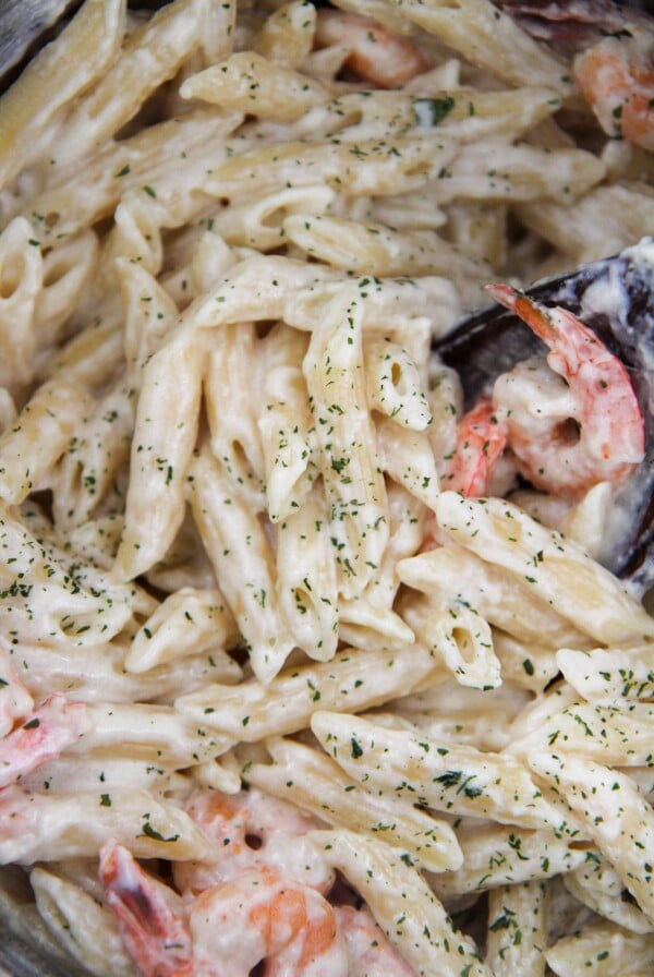 Shrimp and pasta covered in sauce with parsley and a wooden spoon up close.