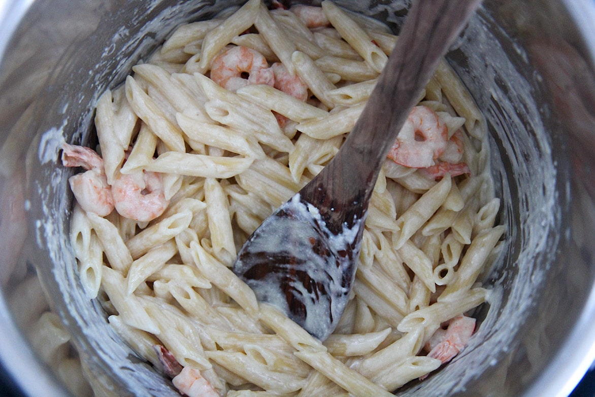 shrimp alfredo penne pasta with a wooden spoon in the instant pot. 