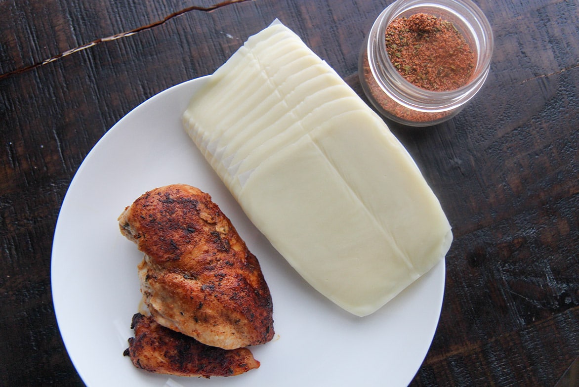 cooked chicken breast, cajun seasoning in a jar, and mozzarella slices. 