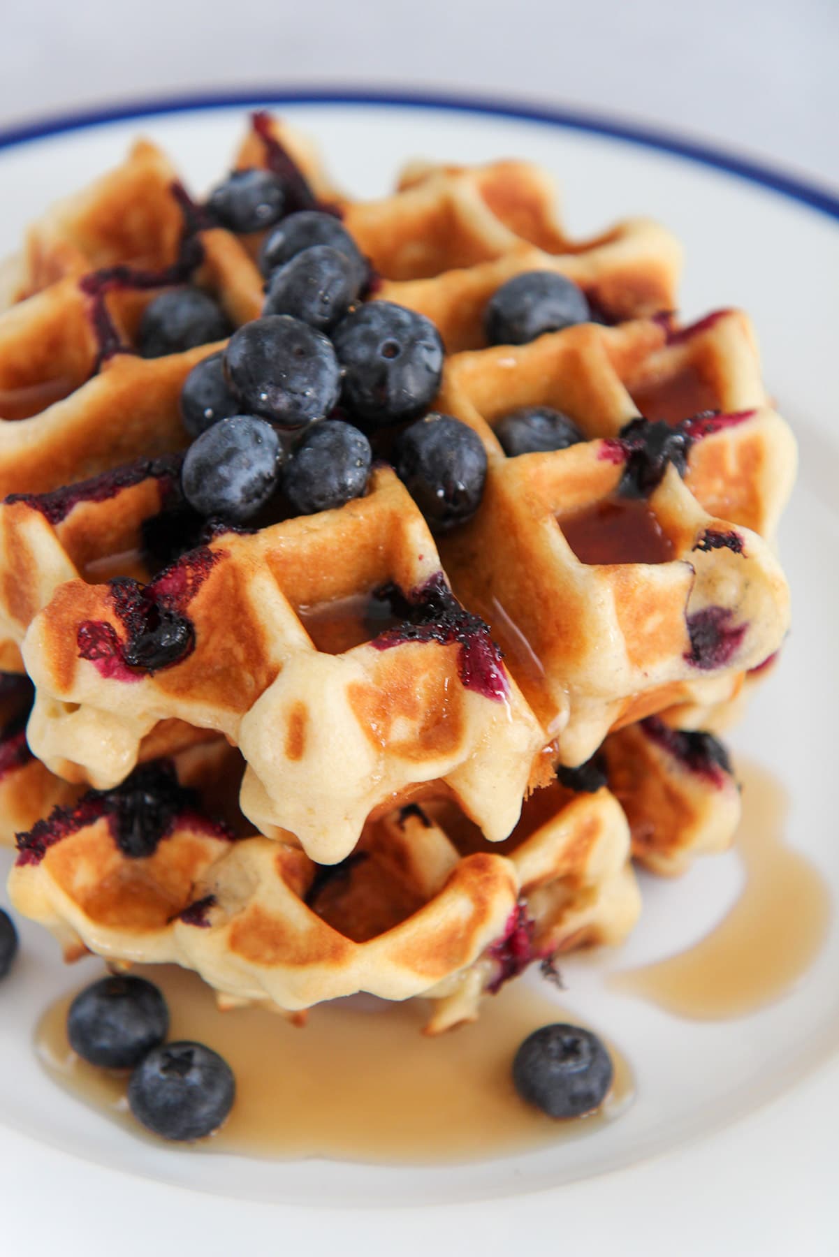 two buttermilk blueberry waffles on a white plate with maple syrup and fresh blueberries. 