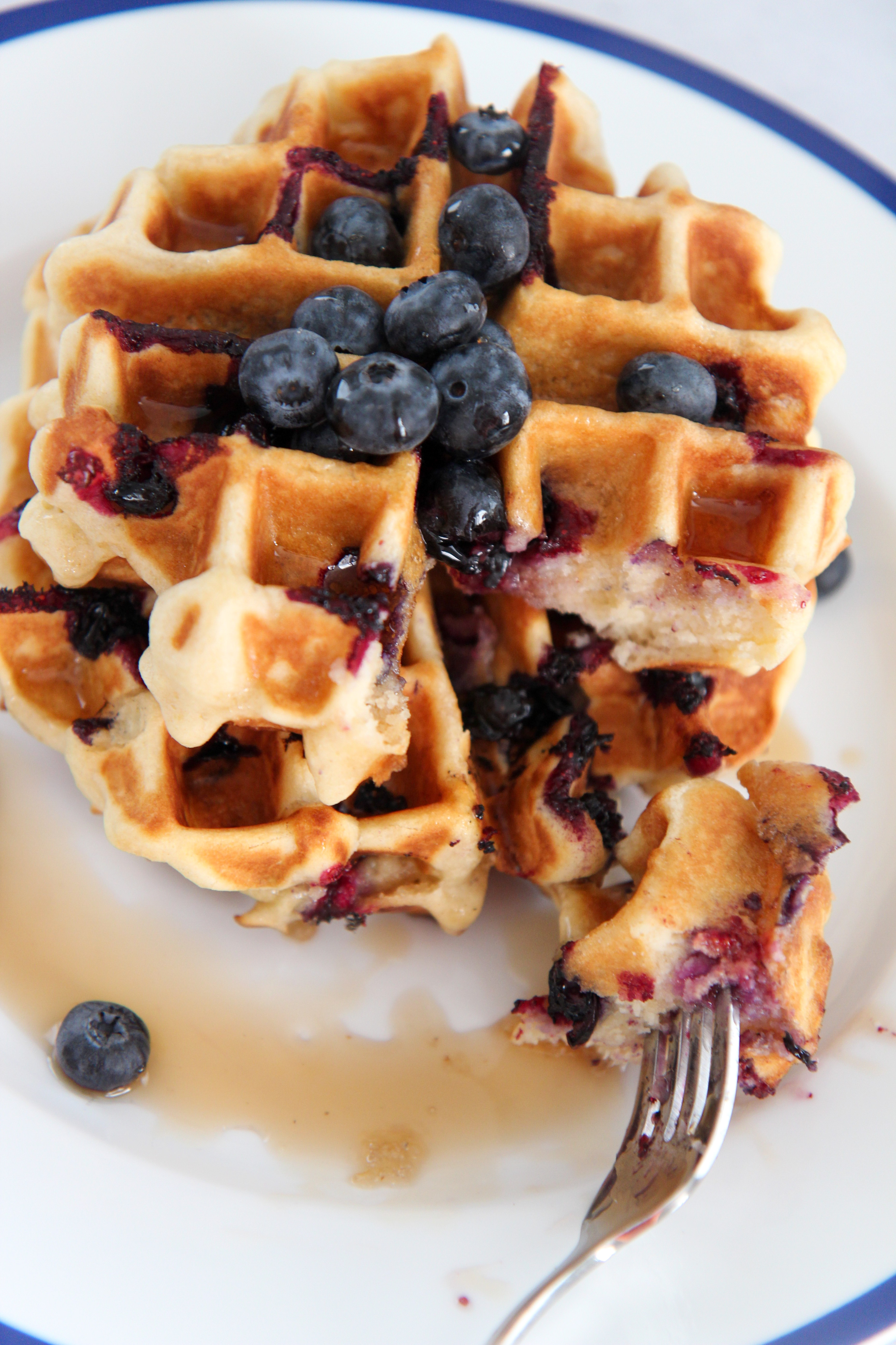 two stacked blueberry waffles with a fork slicing into them. 