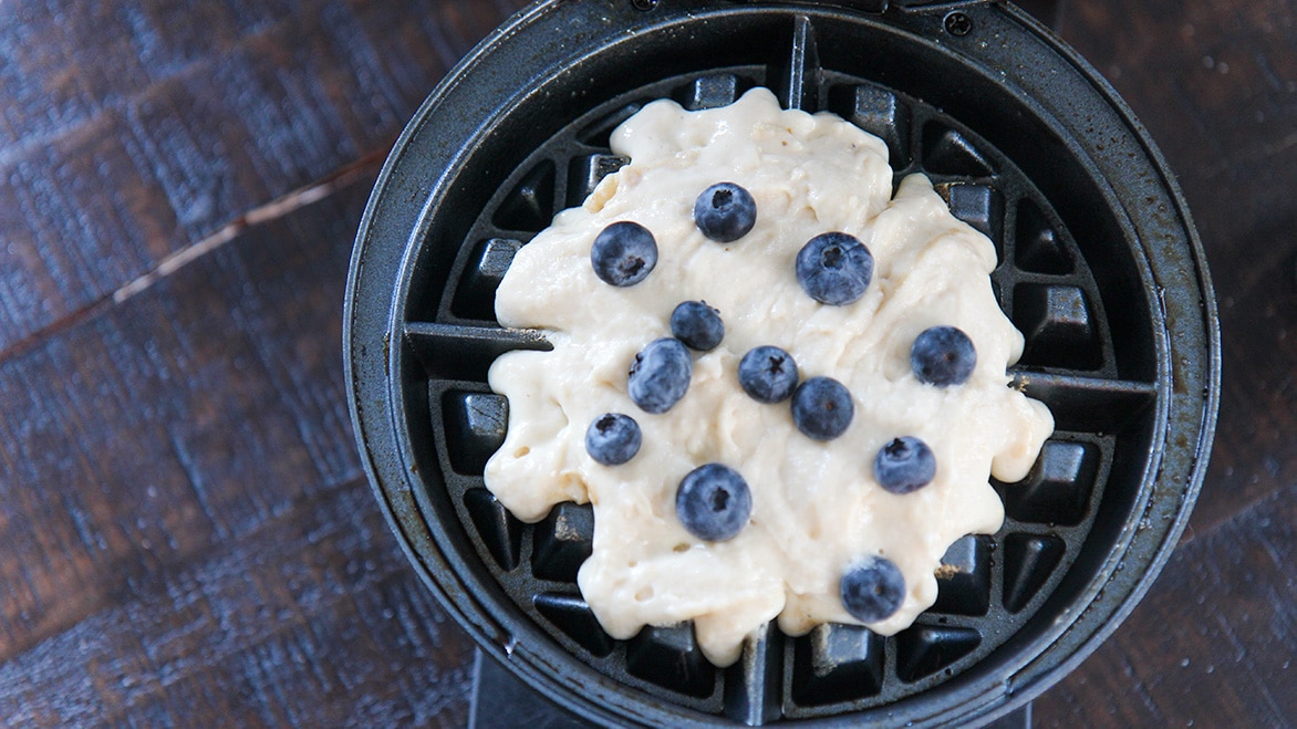 waffle batter and fresh blueberries on a waffle iron. 