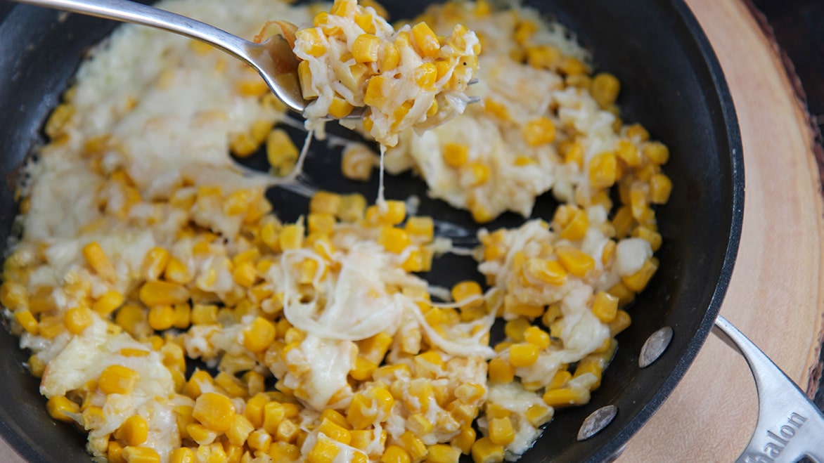 a fork, cheese, and corn in a black skillet.