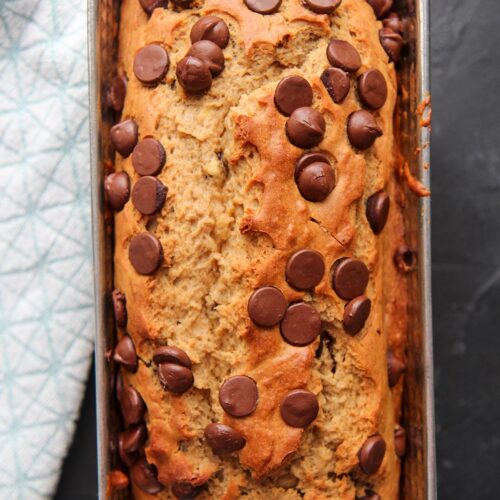 chocolate chip banana bread in a load pan on a black surface with a blue towel on the side.