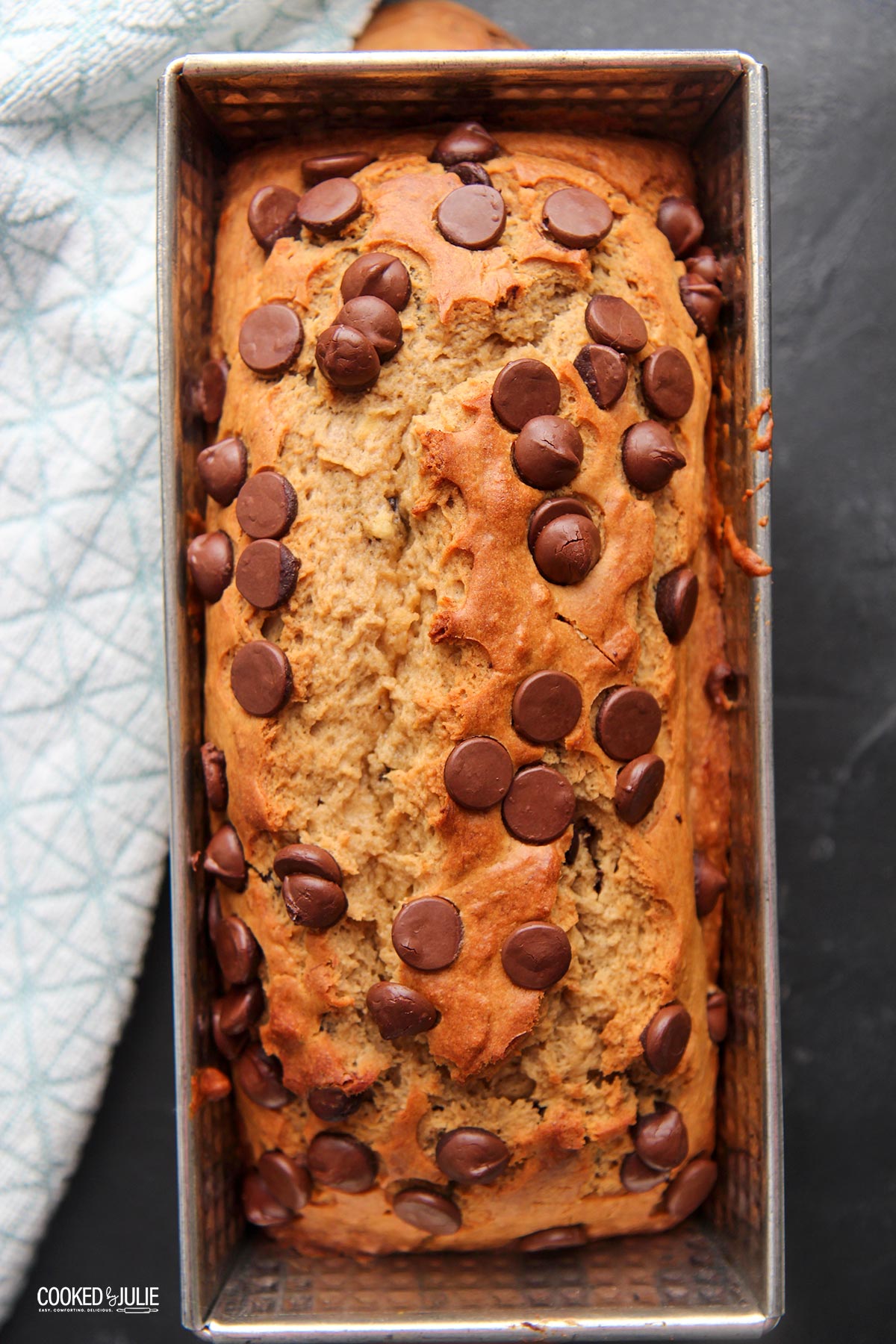 chocolate chip banana bread in a load pan on a black surface with a blue towel on the side.