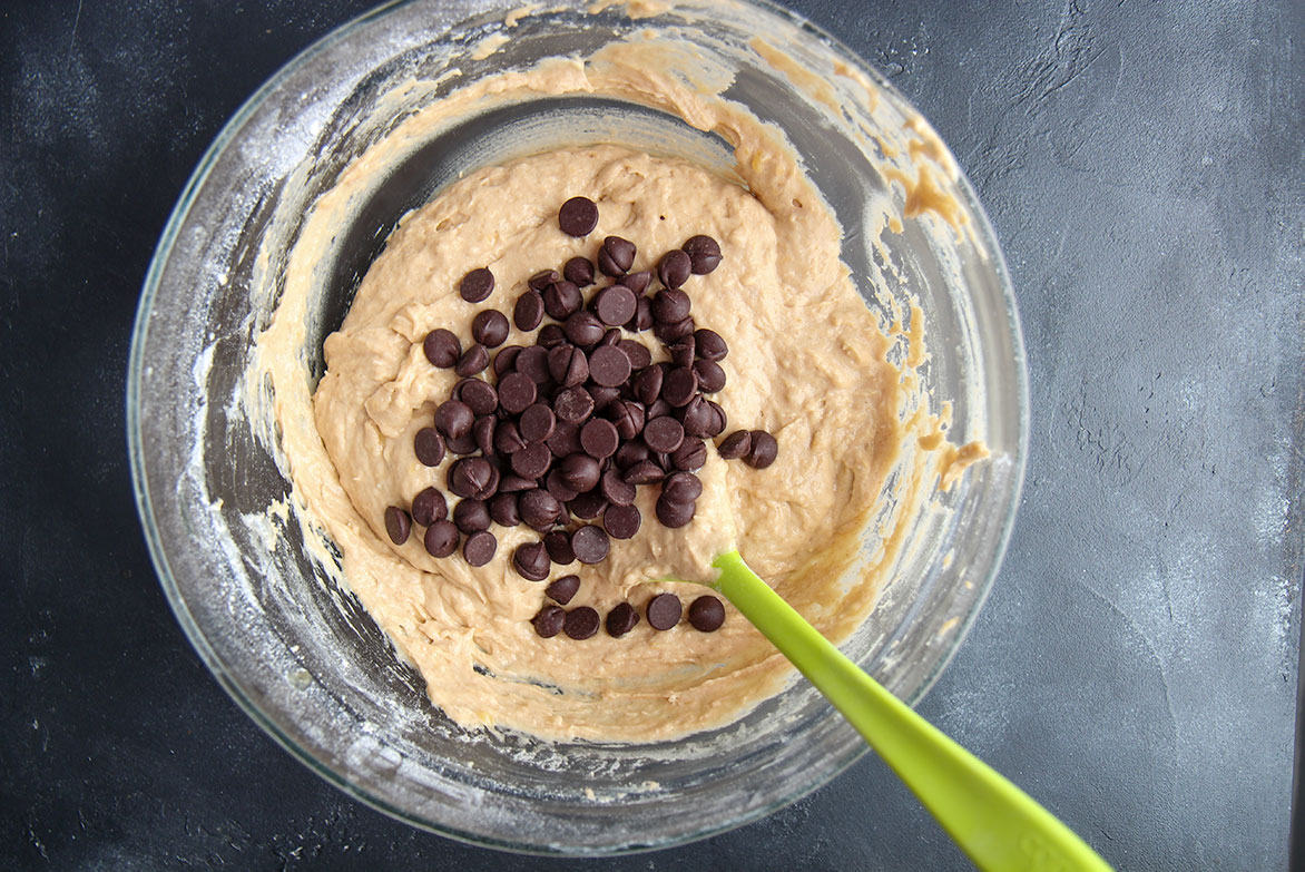 batter with chocolate chips and a green rubber spatula in a bowl. 