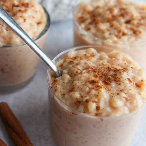 three small bowls with rice pudding and cinnamon sticks on the side.