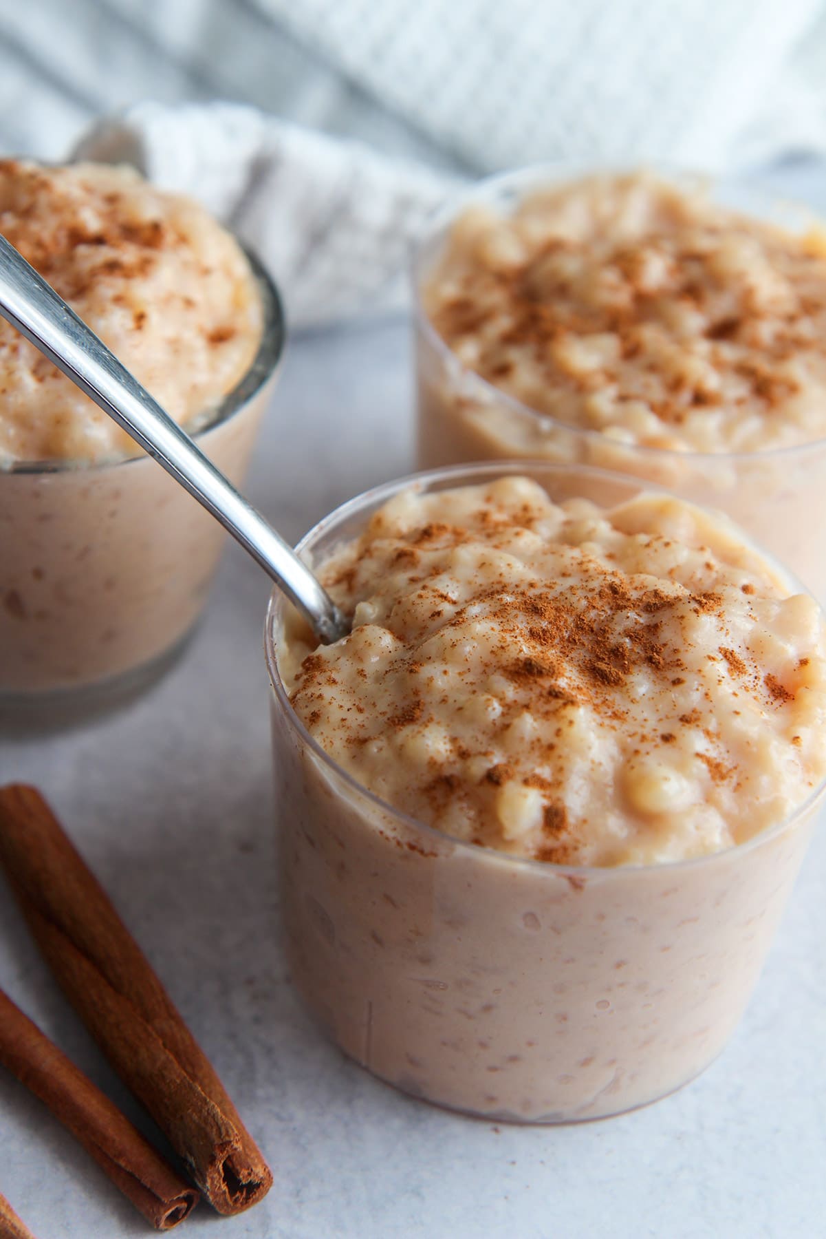 three small bowls with rice pudding and cinnamon sticks on the side.