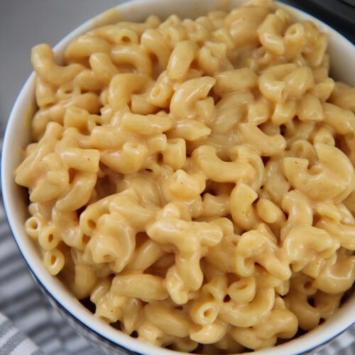 mac and cheese in a white bowl with a gray and white towel on the side.