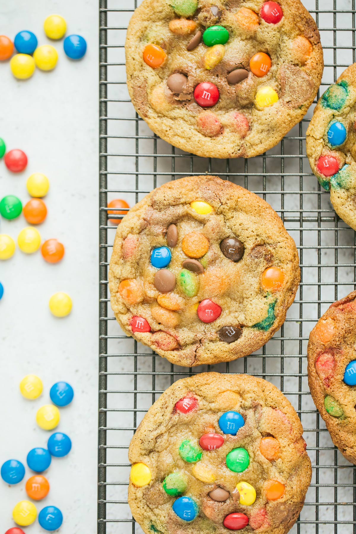 five m&m cookies on a wire rack with m&m candies on the side.