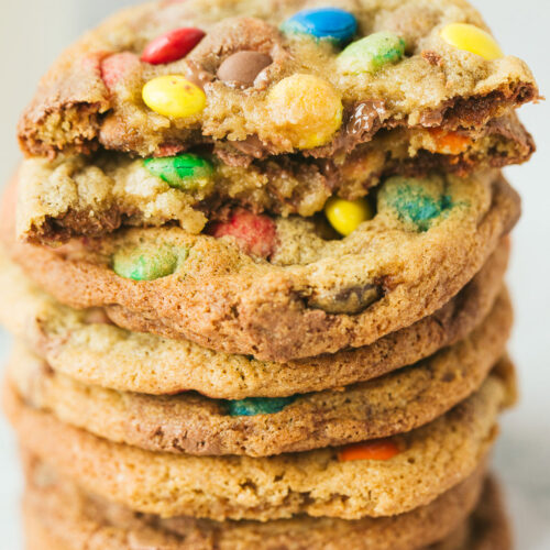 eight m&m cookies stacked on top of each other. One cookie is cut in half.
