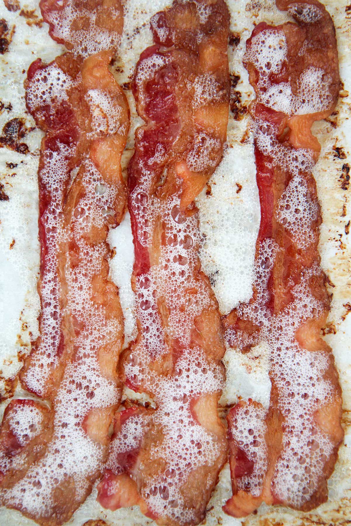 three slices of crispy cooked bacon on a baking sheet. 