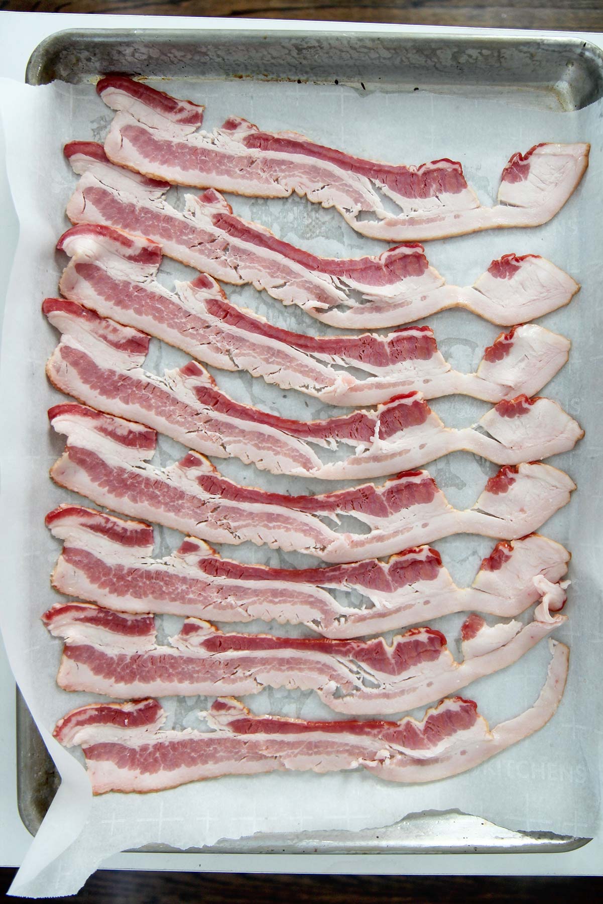 eight slices of raw bacon on a baking sheet lines with parchment paper. 