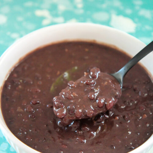 Cuban black beans in a white bowl with a black spoon. On top of a blue and white surface.