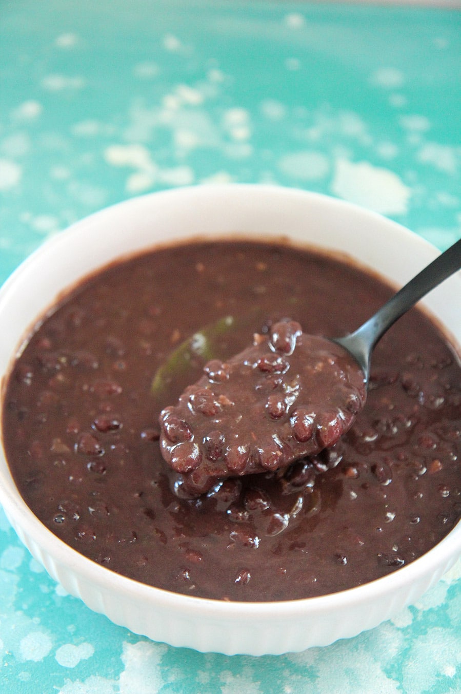 Cuban black beans in a white bowl with a black spoon. On top of a blue and white surface.