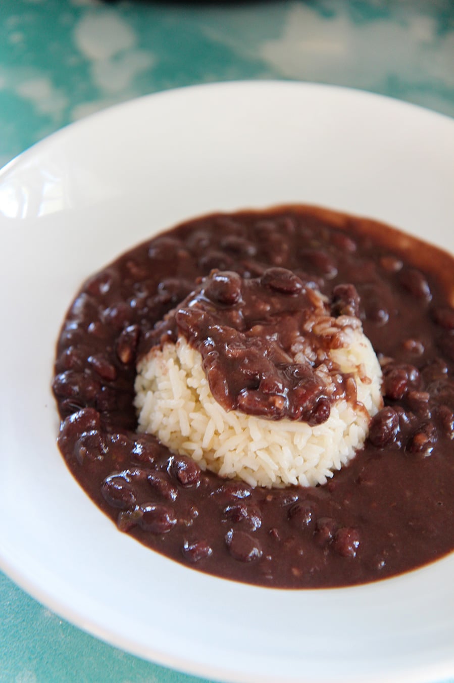 black beans and white rice in a white bowl on top of a blue surface. 