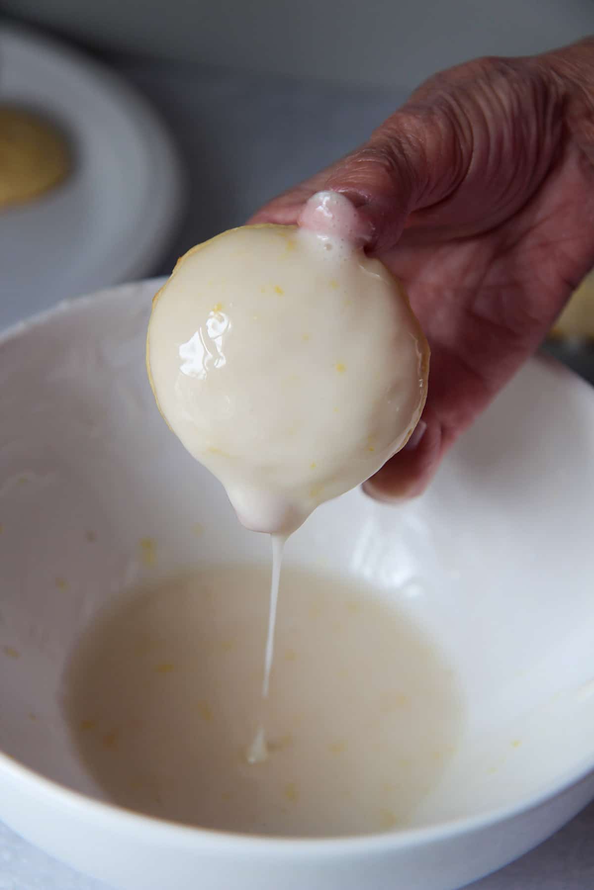 a hand dipping a cookie in a white bowl with glaze. 