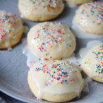 seven Italian lemon ricotta cookies with a glaze and sprinkles on a gray plate.