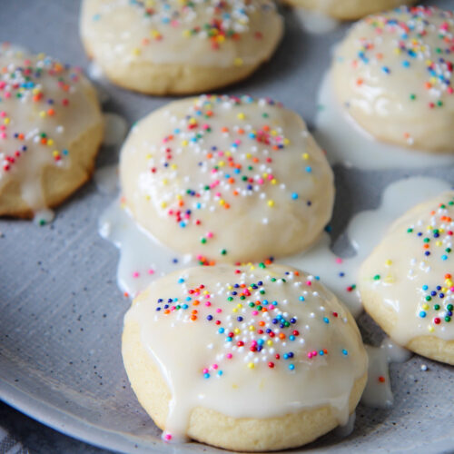 seven Italian lemon ricotta cookies with a glaze and sprinkles on a gray plate.