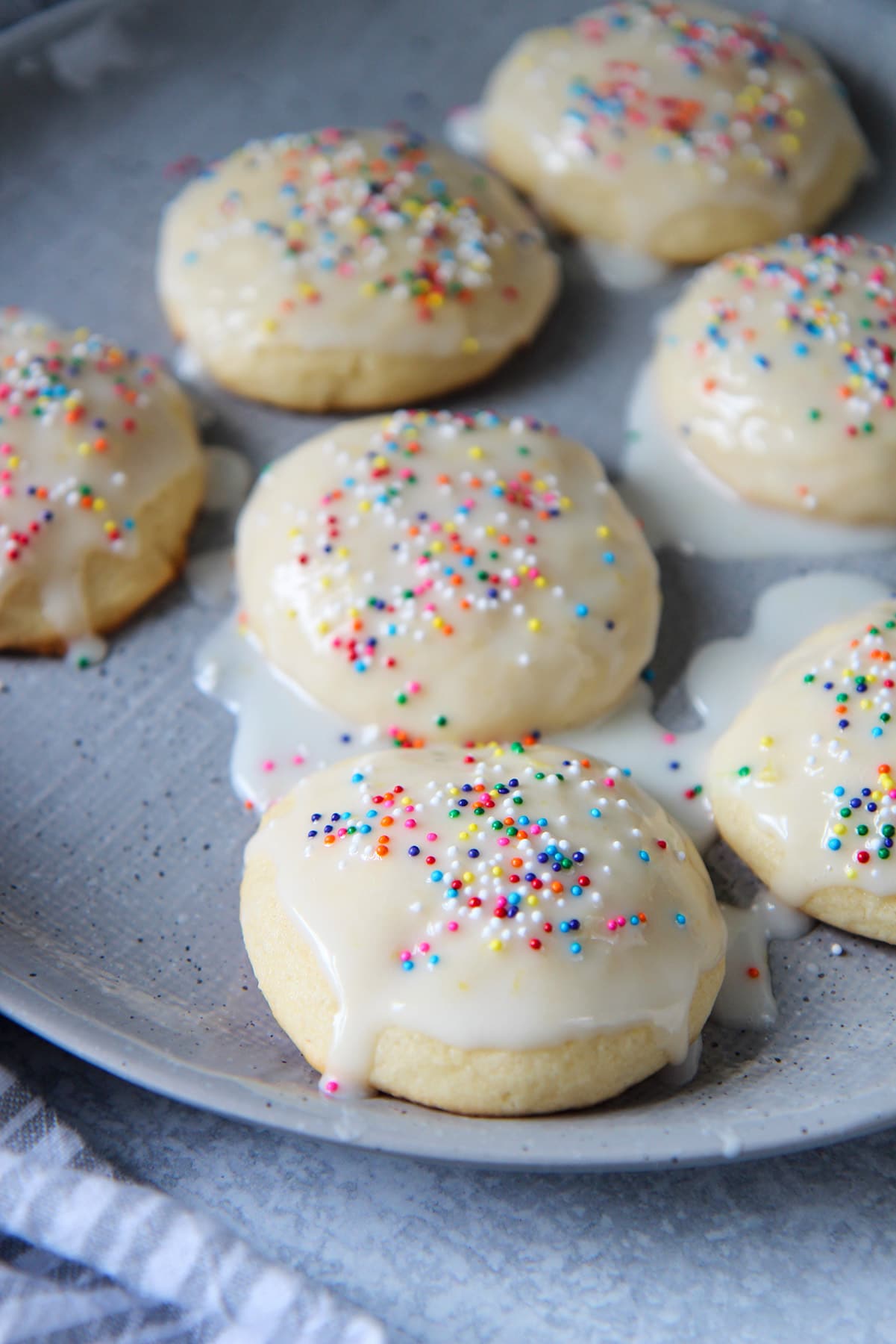 seven Italian lemon ricotta cookies with a glaze and sprinkles on a gray plate. 