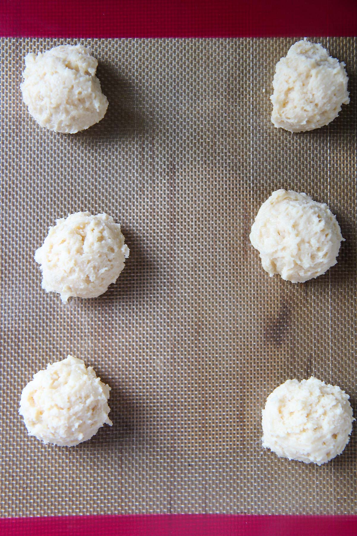 six cookie dough balls on a baking sheet. 