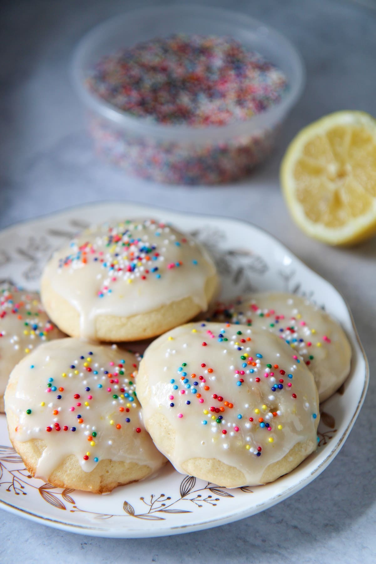 soft baked Italian lemon ricotta cookies on a small plate with sprinkles and a lemon in the background. 