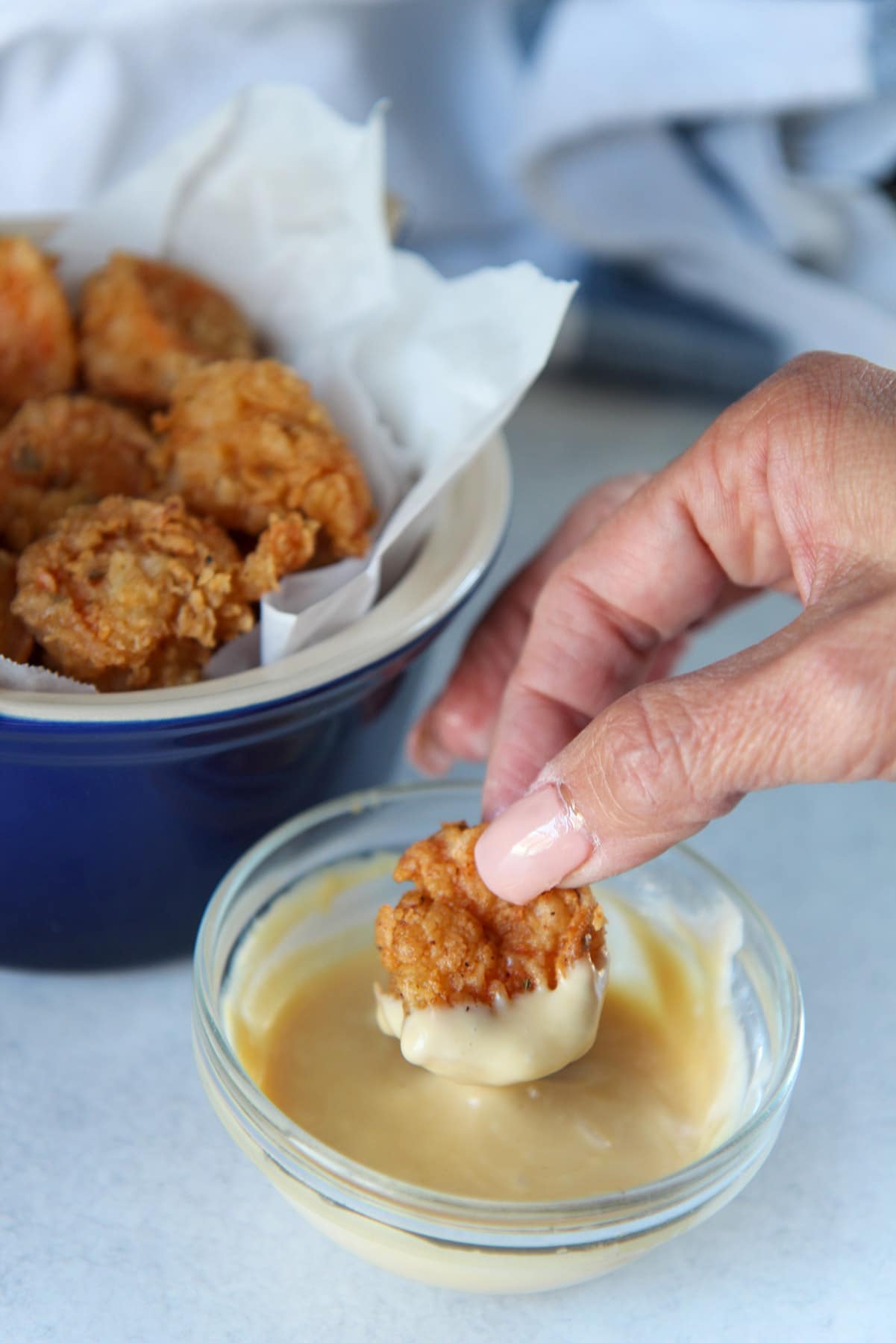 a hand dipping a fried shrimp in a honey mustard sauce. 