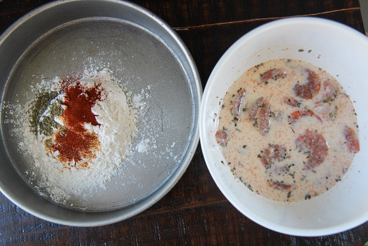 seasoned flour in a cake pan and seafood soaked in milk in a white bowl. 