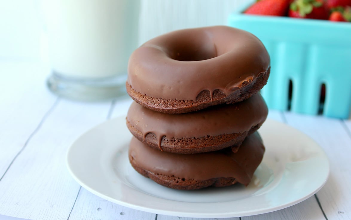 three donuts stacked on top of a white plate with milk and strawberries in the background. 