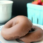 two keto baked chocolate donuts on a white plate with a basket of strawberries in the background.