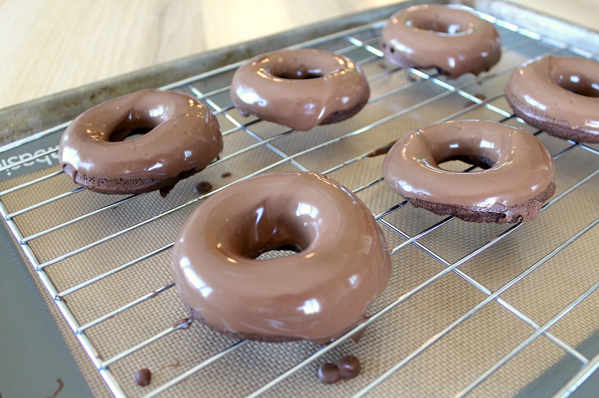 six glazed chocolate donuts on a wire rack 