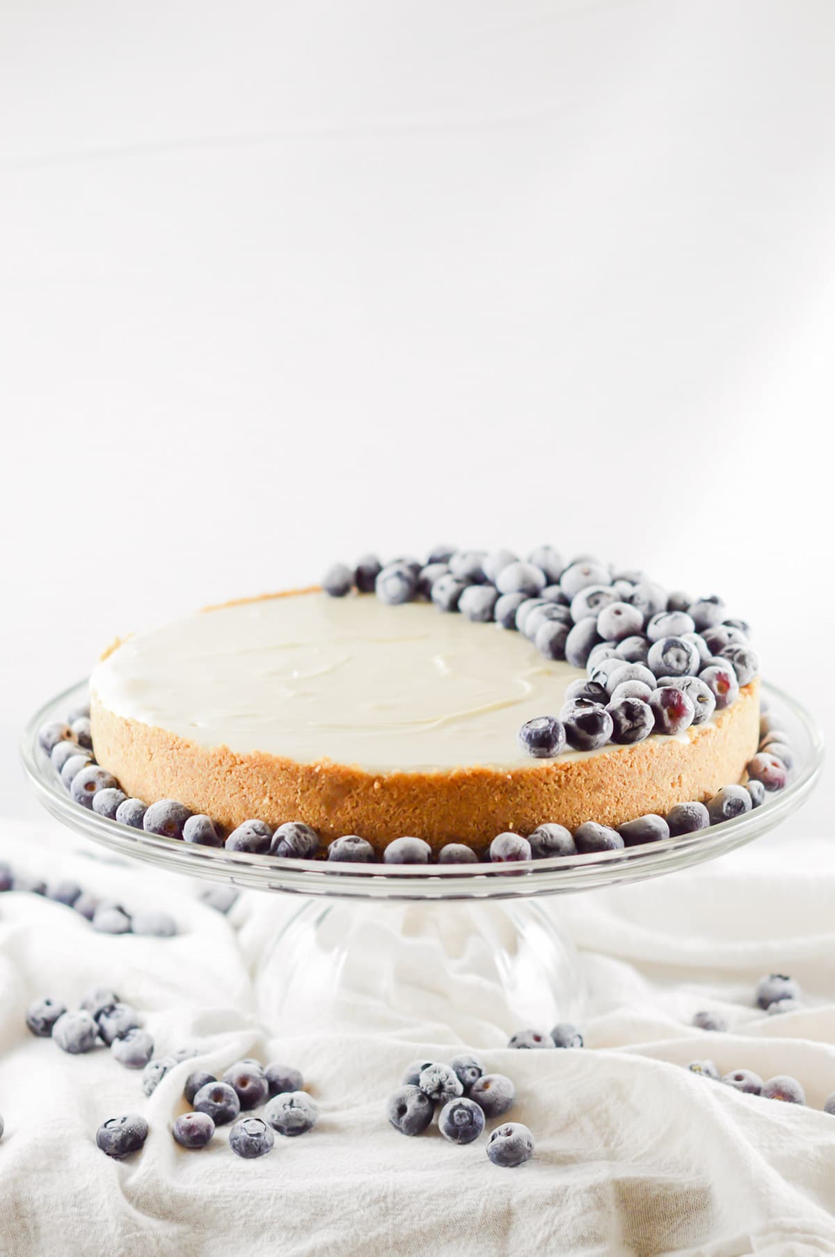 a whole plain no bake cheesecake on a cake stand decorated with fresh blueberries.