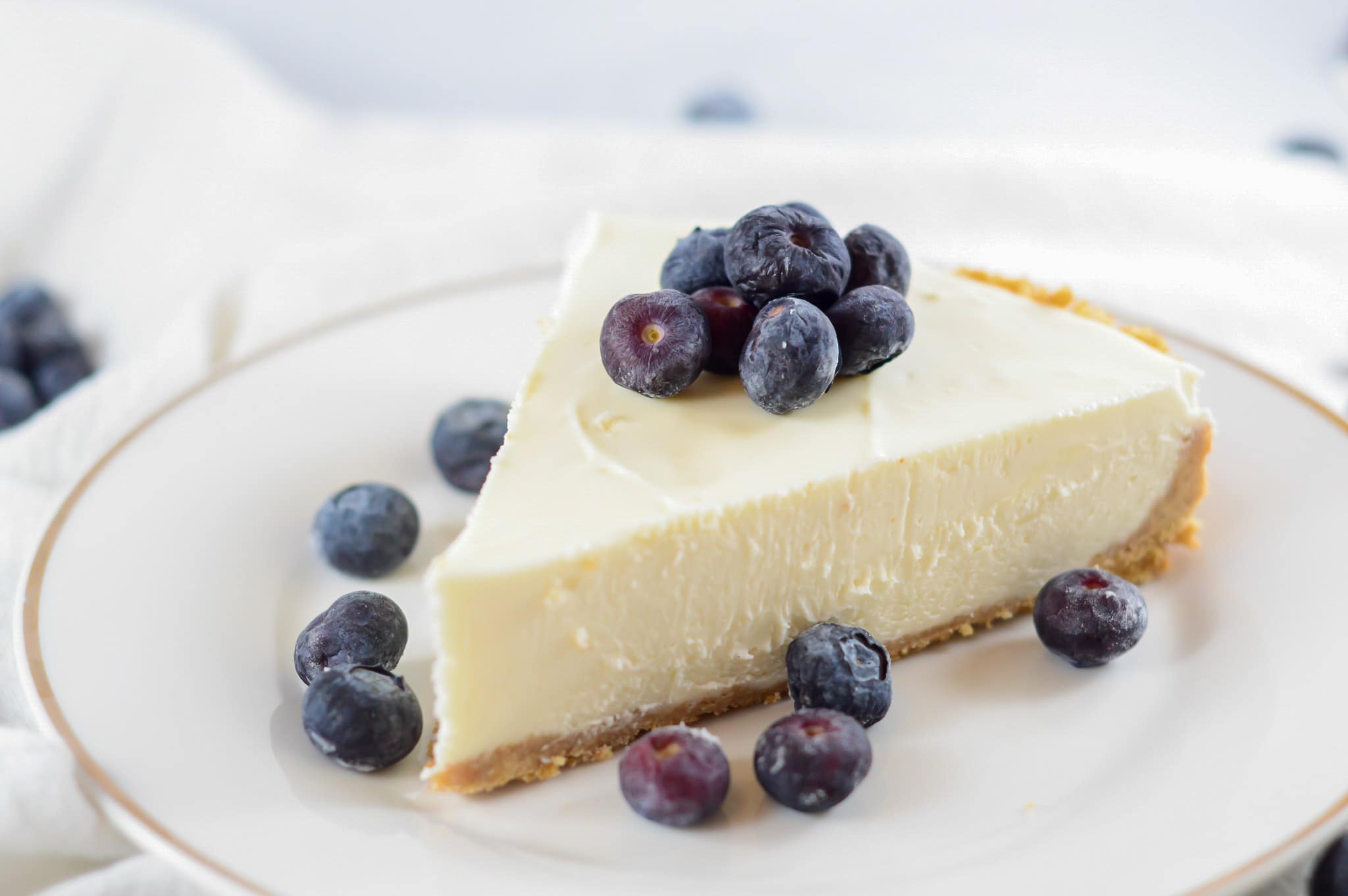 a slice of no-bake cheesecake on a white plate with fresh blueberries.