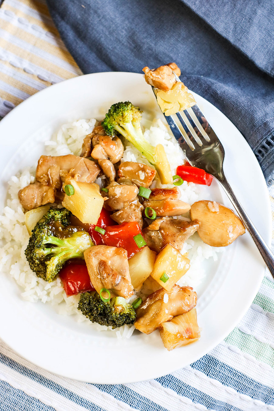 chicken, vegetables, fruit, and white rice on a white plate with a fork. 