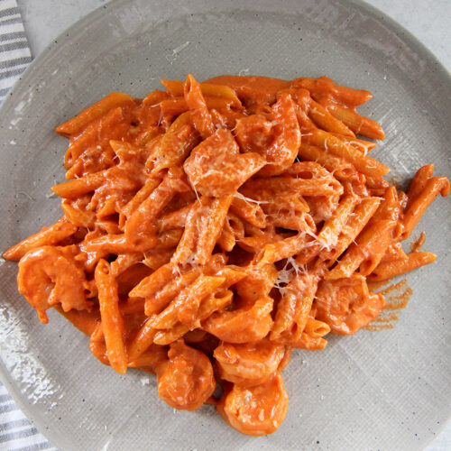 penne alla vodka with shrimp on a gray plate with a gray and white towel on the side.