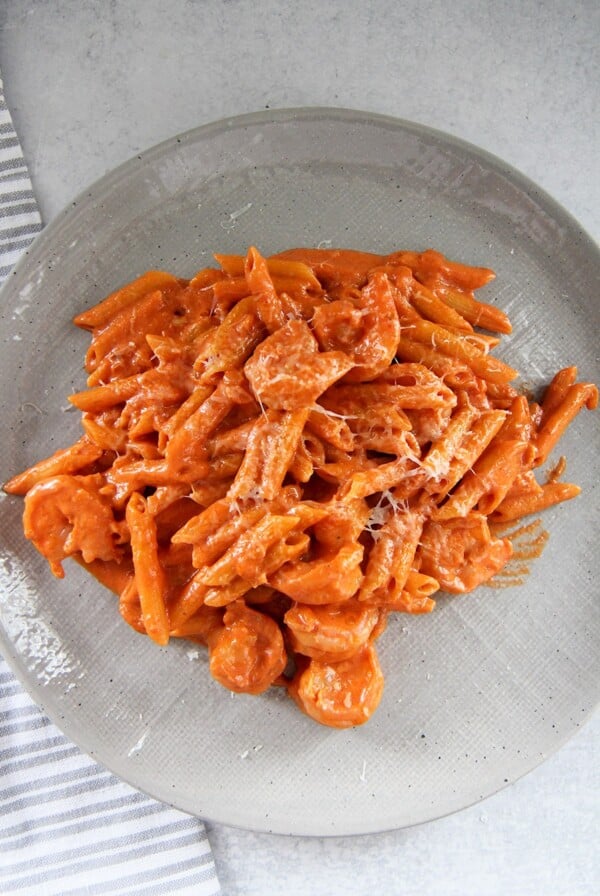 penne alla vodka with shrimp on a gray plate with a gray and white towel on the side.