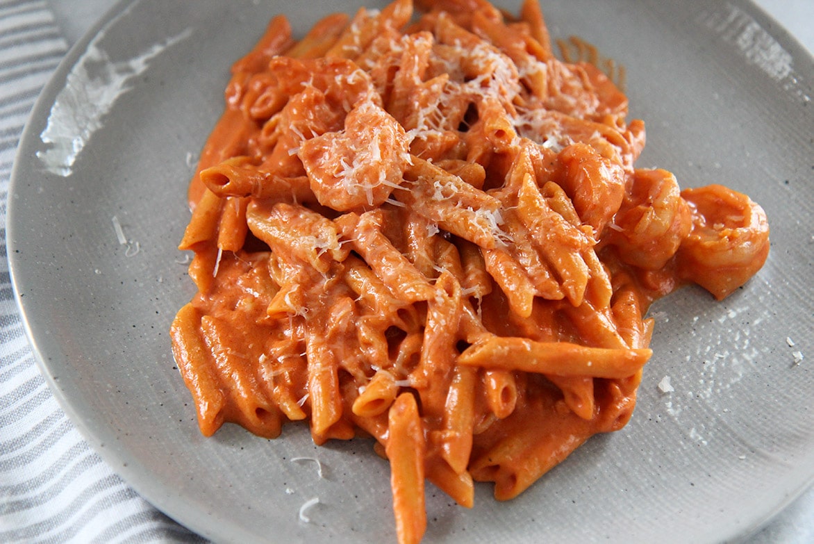 pasta, shrimp, sauce, and parmesan cheese on a gray plate up close. 