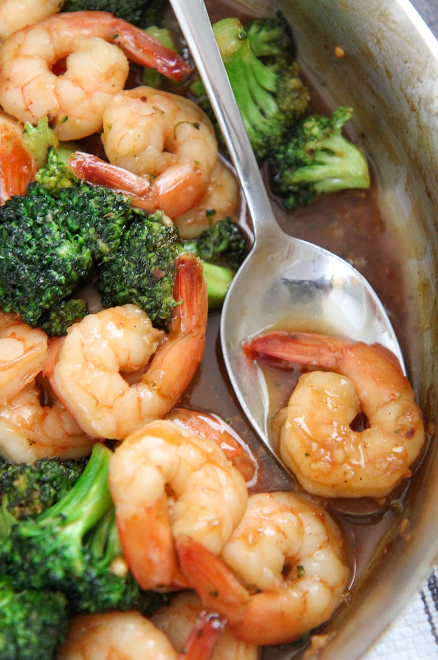 spicy honey shrimp and broccoli in a skillet with a spoon holding one shrimp. 