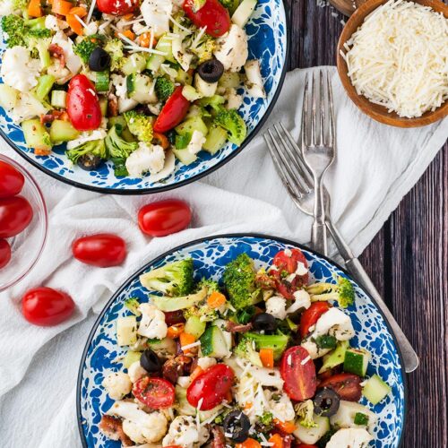 two bowls filled with vegetable salad with homemade Italian dressing. Two forks on the side and parmesan cheese.