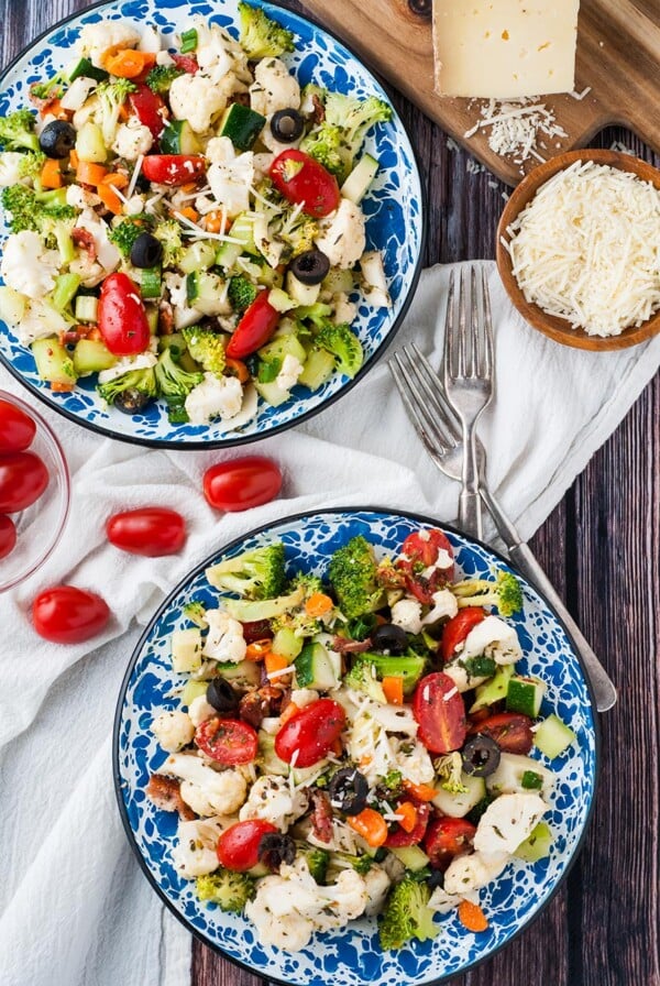 two bowls filled with vegetable salad with homemade Italian dressing. Two forks on the side and parmesan cheese.