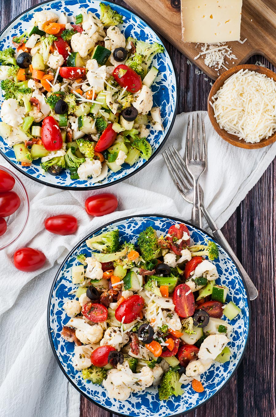 two bowls filled with vegetable salad with homemade Italian dressing. Two forks on the side and parmesan cheese.