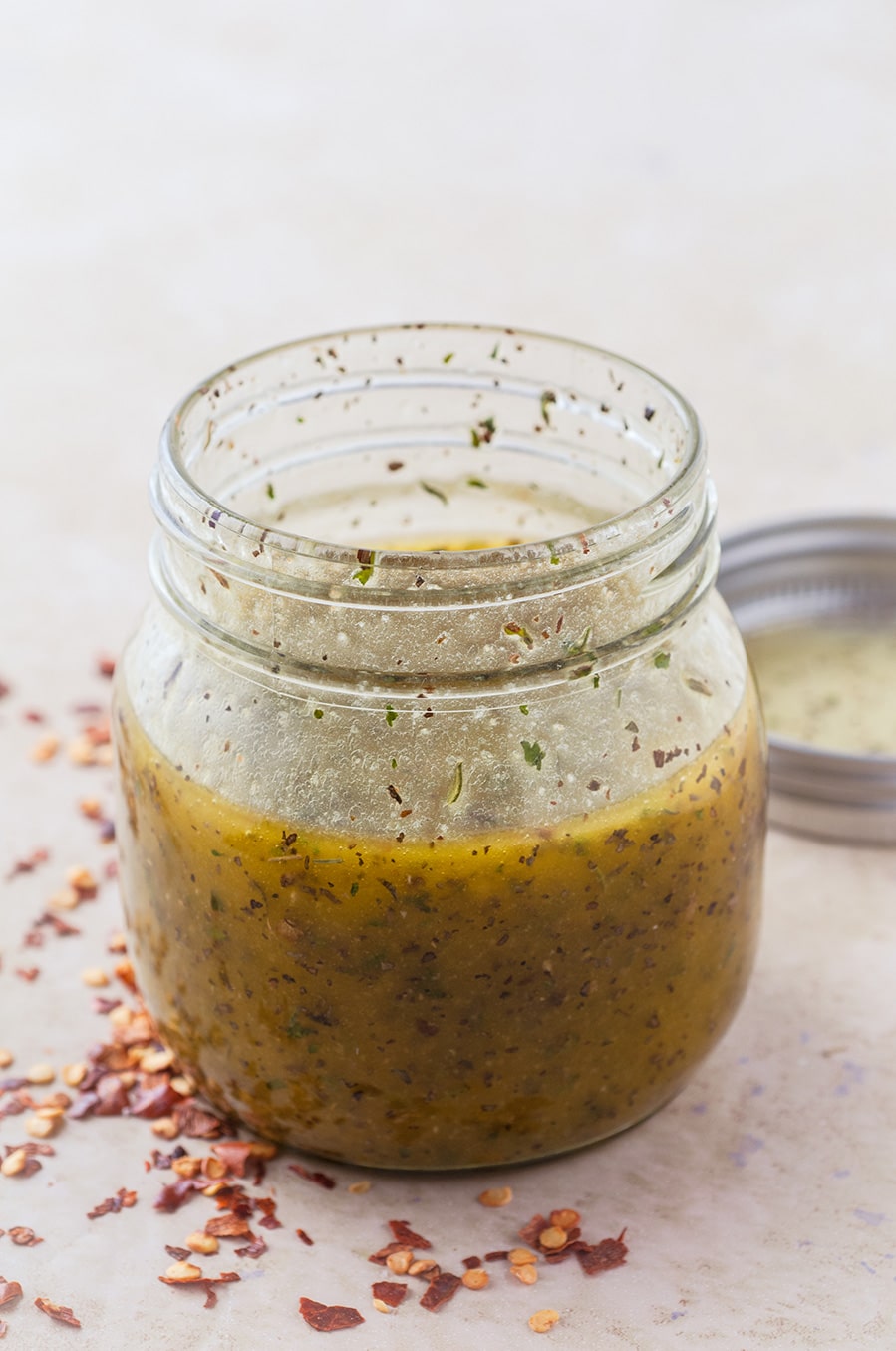 a small mason jar with dressing in it. Red crushed pepper and a lid on the side. 